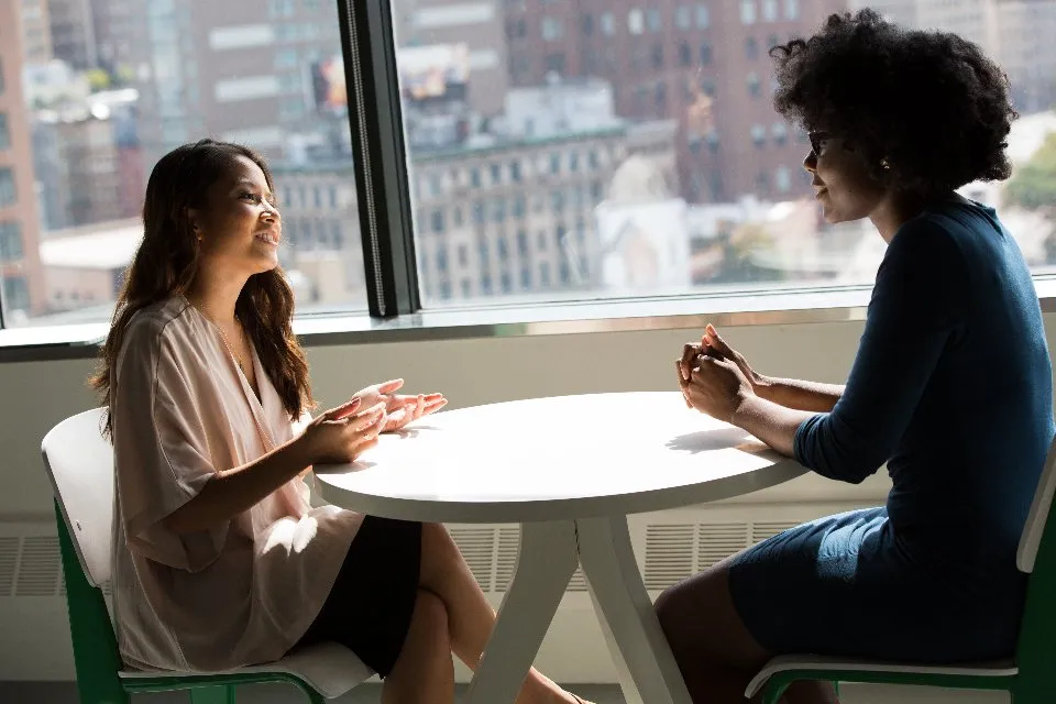 Dos mujeres conversando en una mesa junto a un ventanal